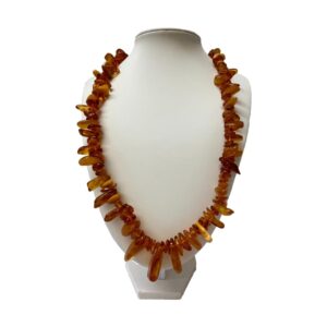 Main photo of vintage Baltic amber necklace displayed on a display stand and forward facing. The amber pieces are not uniform in size and have a tribal look with long pieces sticking out like teeth. Most of the amber is cognac colour with very few egg yolk and butterscotch pieces. The necklace is quite long and covers most of the front of the display stand.