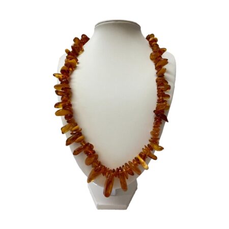 Main photo of vintage Baltic amber necklace displayed on a display stand and forward facing. The amber pieces are not uniform in size and have a tribal look with long pieces sticking out like teeth. Most of the amber is cognac colour with very few egg yolk and butterscotch pieces. The necklace is quite long and covers most of the front of the display stand.