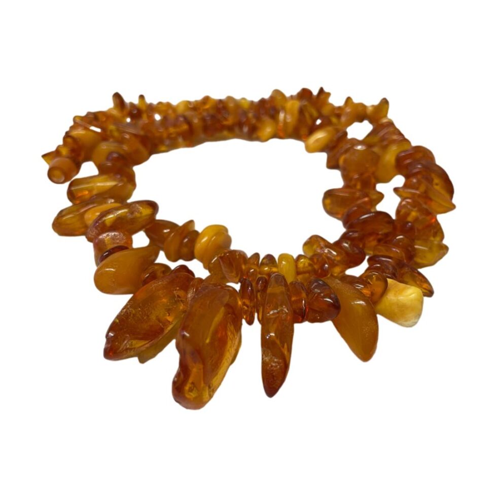 Photo of the amber necklace wound round itself once and placed on a flat surface. The large 'teeth' like amber pieces are mostly in the foreground.