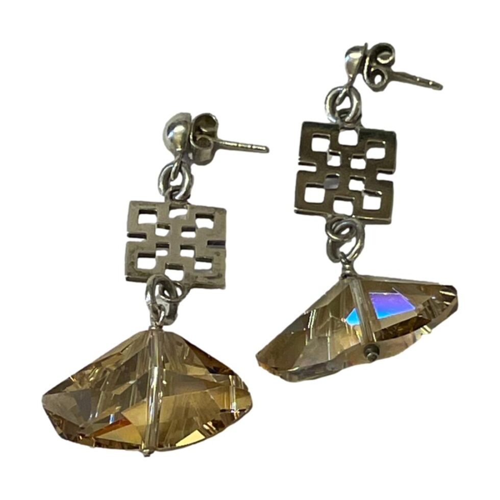 Photo of both earrings laid side by side on a flat surface. The light is hitting the quartz crystal and some bright colours are bouncing off the quartz - especially earing on right which is flashing purple/blue/turquoise to one facet.