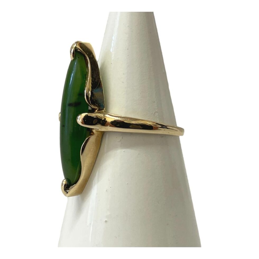 Photo of jade ring still displayed on a cone shaped stand this time with the ring front facing left and showing the unusual setting for this long slim jade stone.