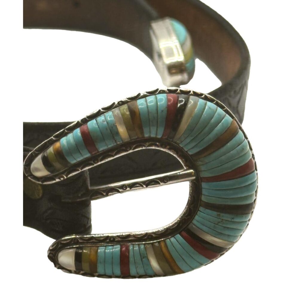 Close up photo of the belt buckle which is fully inlaid with mostly turquoise intermittently divided with mother-of-pearl, coral, onyx, tigers eye & possibly agate. All the inlaid pieces on buckle, tip & loops are long thin strips.