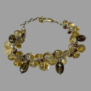 Main photo of silver quartz crystal bracelet displayed on a flat surface with the clasp closed and bracelet laid out in a circle. The clasp is in the background and closed to the last extended chain link. The bracelet is a link chain body with multiple smooth and faceted quartz crystal beads added.