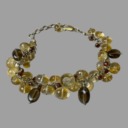 Main photo of silver quartz crystal bracelet displayed on a flat surface with the clasp closed and bracelet laid out in a circle. The clasp is in the background and closed to the last extended chain link. The bracelet is a link chain body with multiple smooth and faceted quartz crystal beads added.