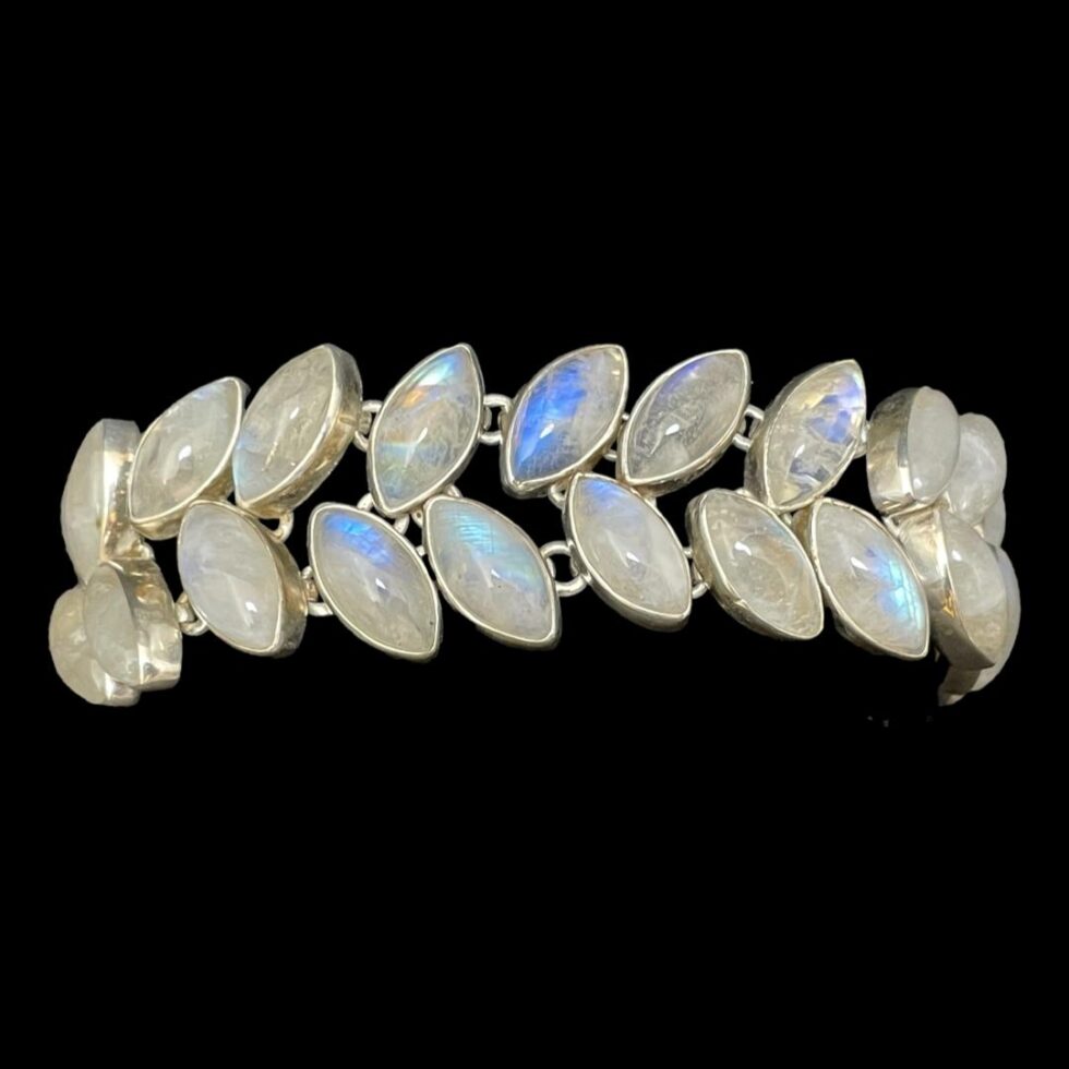 Main photo of vintage rainbow moonstone bracelet displayed around a black display cushion against a black background. The stones to the centre are the most vibrant blue with the others white with hints of blue. The top row of stones is leaning to the right and lower row is leaning to the left.