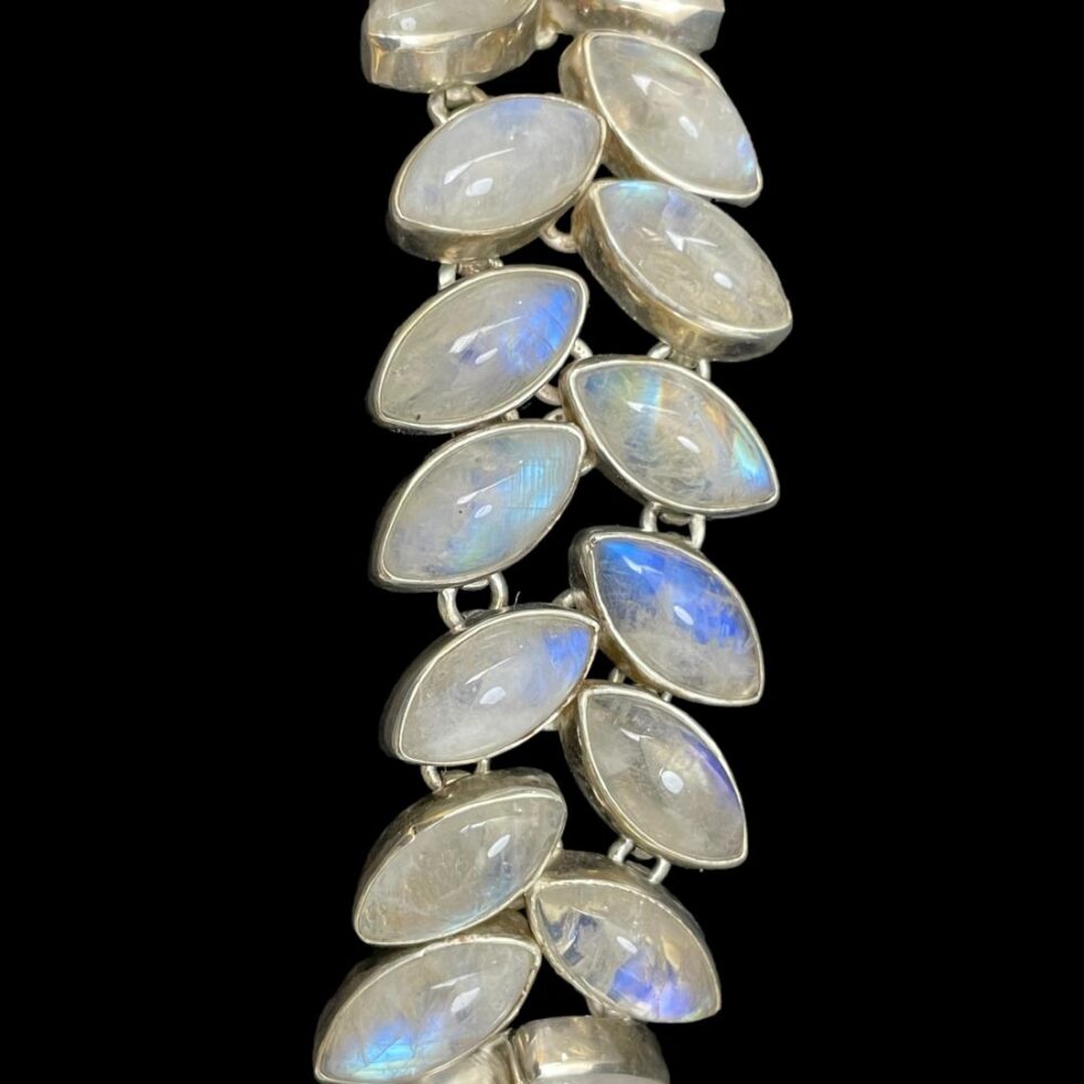 A close up photo of the middle segment of the bracelet which is laid vertically against a black background. The blue hues are coming through beautifully here and there is even one stone which appears to be rainbow colours!