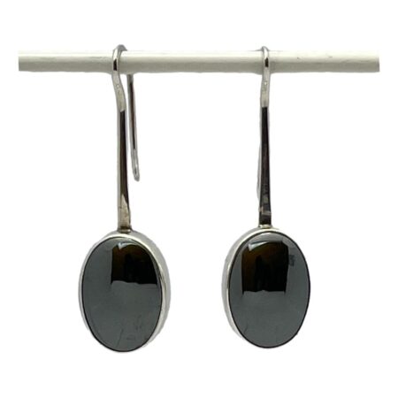 Main photo of Modernist silver hematite earrings displayed hanging side by side against a white background. The simplistic design has long hook fasteners which extend at the front to form the frame housing the hematite stones. The stones are a generous size and have a mirror effect (hence mirroring what lies ahead - one of the stones properties) Very sleek and sassy pair of earrings.