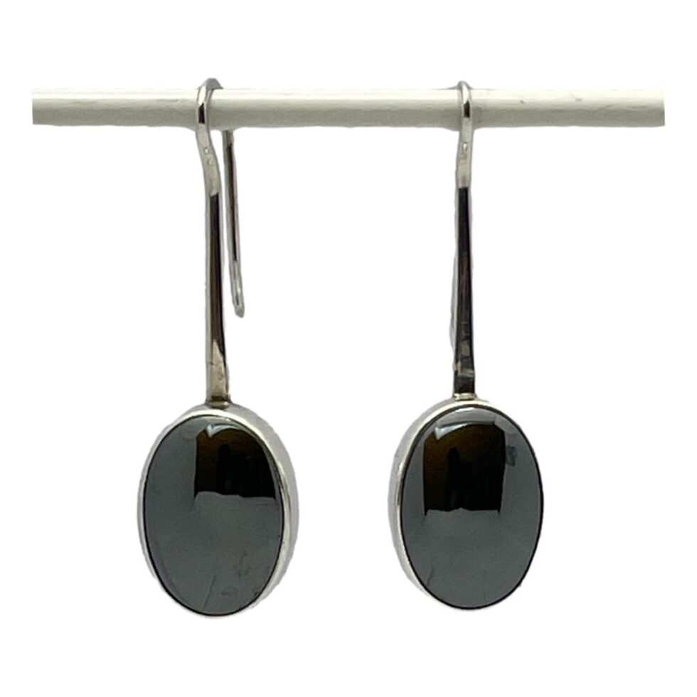 Main photo of Modernist silver hematite earrings displayed hanging side by side against a white background. The simplistic design has long hook fasteners which extend at the front to form the frame housing the hematite stones. The stones are a generous size and have a mirror effect (hence mirroring what lies ahead - one of the stones properties) Very sleek and sassy pair of earrings.