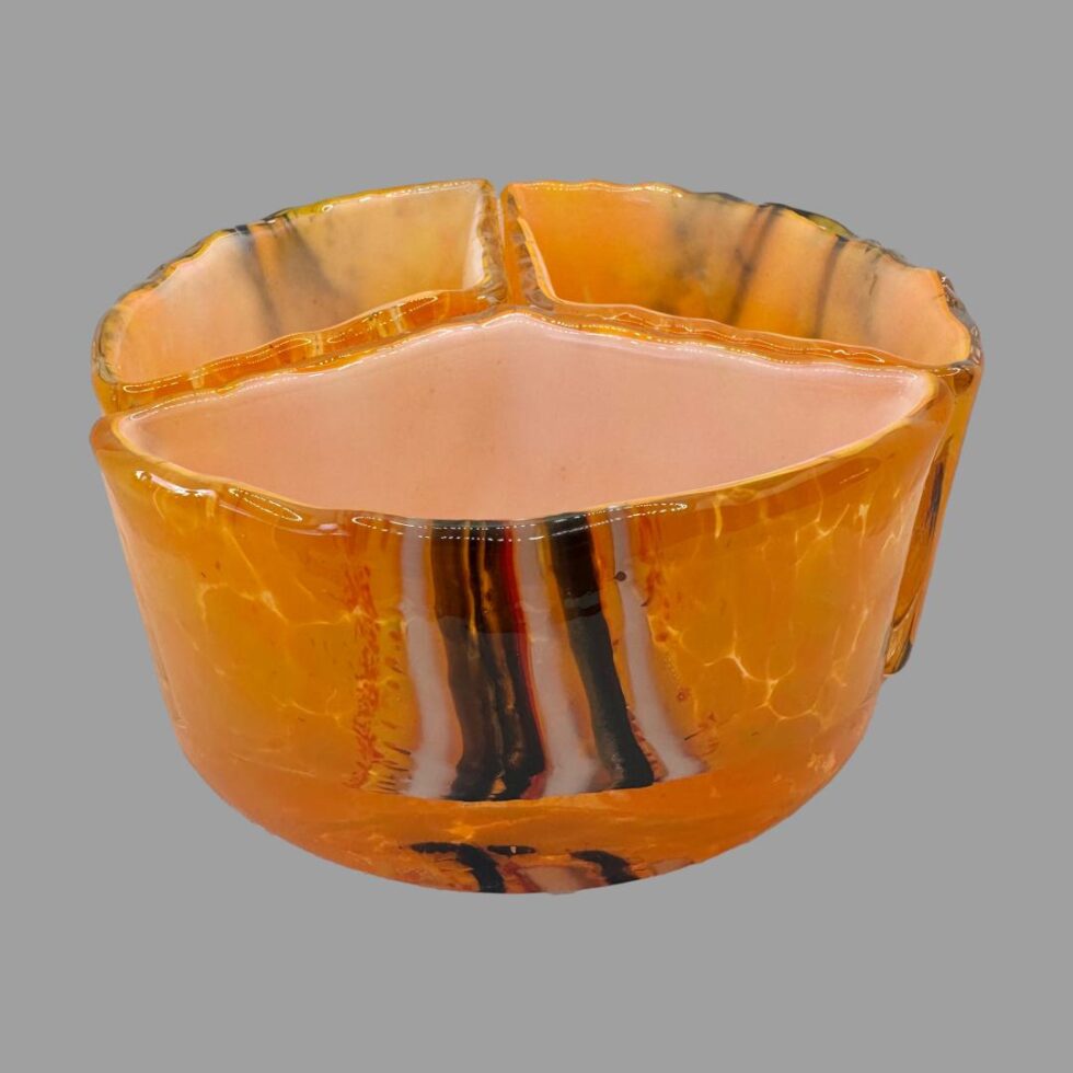 Main photo of Milan Nosek nest of bowls art glass showing all three pieces laid out a circle with each third creating the whole., The overall colour is a vibrant orange with brown and white vertical strips around the centre area of bowl exterior. Each segment of bowl has different strips.