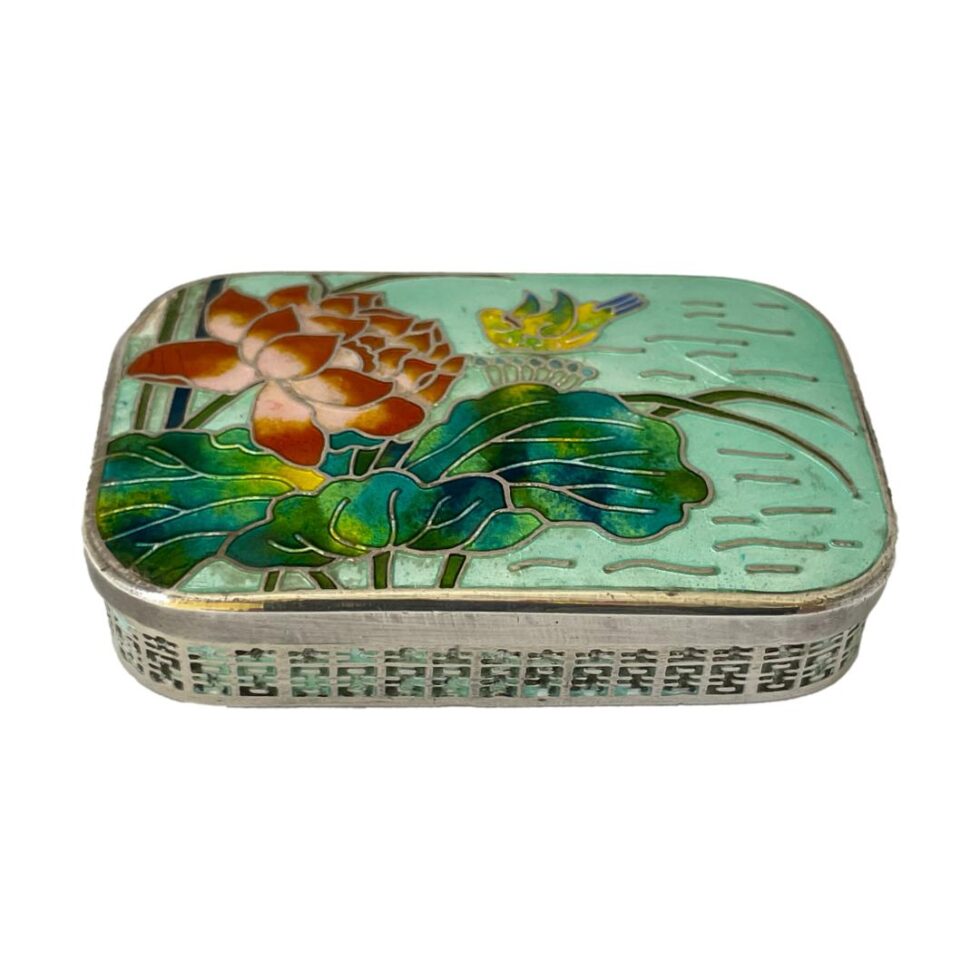 Main photo of Korean silver &enamel box displayed on a flat surface and seen from a little height looking diagonally down. Sadly not in perfect condition, this box is still stunning to behold and equally very usable. The colours of the enamel on the lid are incredibly eye catching with the red lotus flower to the top left, the yellow water fowl to top centre, lovely green blue colours of the lotus leaves which cover almost all the lower part of the image then pale green blue colour of the water to the right.