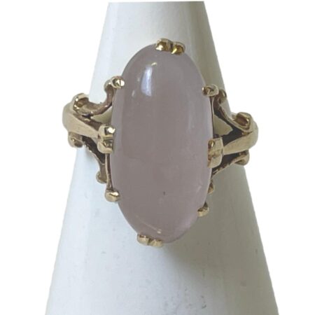 Main photo of Gold rose quartz ring displayed on a cone shaped stand with the ring front forward facing. The rose quartz cabochon is a generous oval size and beautifully polished. It is securely clawed in place with double claws to the top, bottom and sides and additional single claws in between these. The cloudy pale pink of the rose quartz and the 9 karat yellow gold marry together very well.