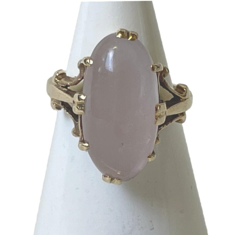 Main photo of Gold rose quartz ring displayed on a cone shaped stand with the ring front forward facing. The rose quartz cabochon is a generous oval size and beautifully polished. It is securely clawed in place with double claws to the top, bottom and sides and additional single claws in between these. The cloudy pale pink of the rose quartz and the 9 karat yellow gold marry together very well.
