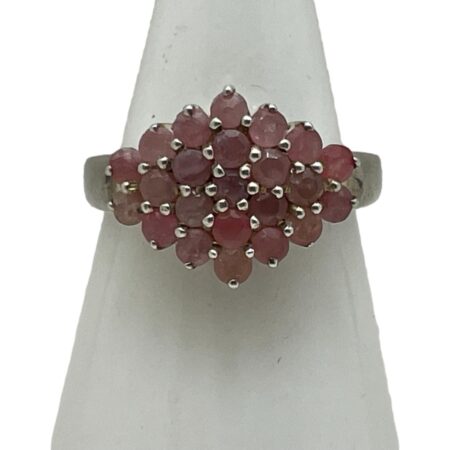 Main photo of silver ruby cluster ring displayed on a white cone shaped stand and seen with the ring front forward facing. This is quite an unusual ring in that the cluster is side wide rather than circular. The rubies are a sweet pale pink and red colour mix which marries well with the silver.