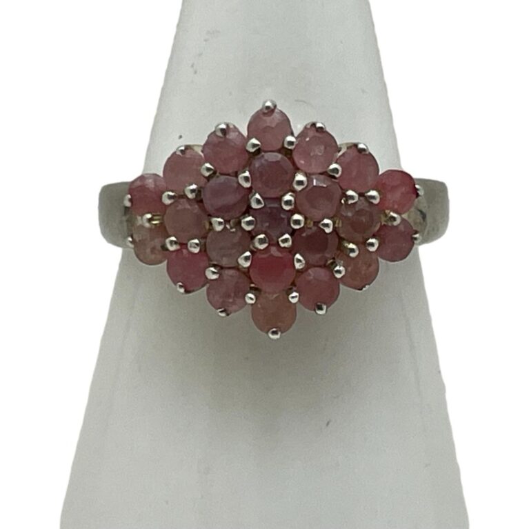 Main photo of silver ruby cluster ring displayed on a white cone shaped stand and seen with the ring front forward facing. This is quite an unusual ring in that the cluster is side wide rather than circular. The rubies are a sweet pale pink and red colour mix which marries well with the silver.