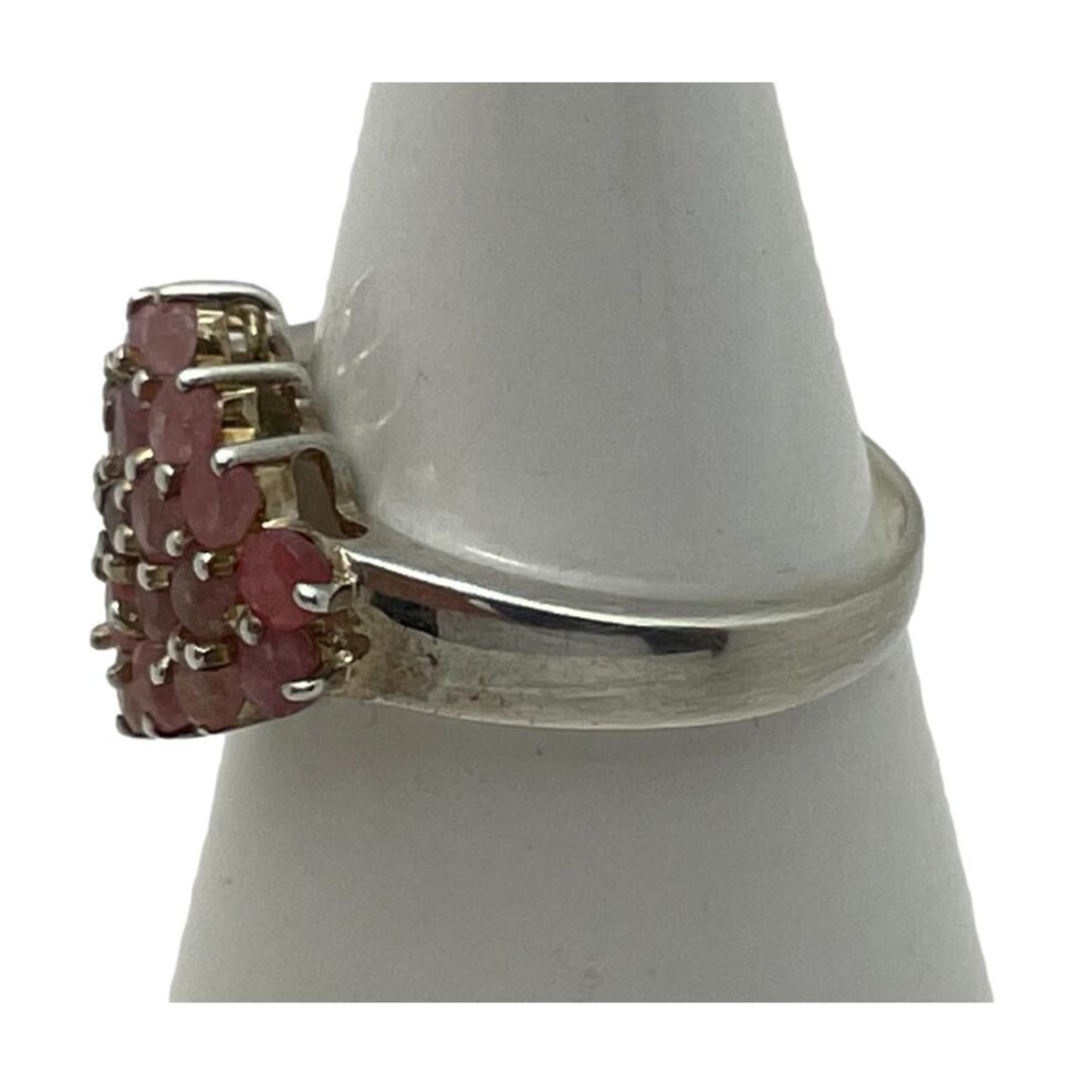 Photo of silver ruby cluster ring still displayed on a cone shaped stand with the ring front facing left to reveal the solid but plain shoulder.