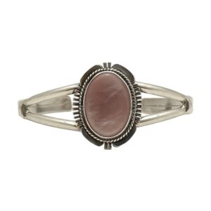 Main photo of Navajo signed cuff bracelet displayed on a flat surface against a white background with the front of bracelet at centre and forward facing. The cuff has a split band at front with an oval central frame which houses the dusky pink coloured natural shell. The frame is a very recognisable Navajo design with 'feathered' edges at the 4 compass points and intricate rope twist around the stone.