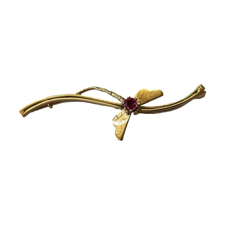 Main photo of gold garnet dragonfly brooch displayed horizontally long against a white background. The bar of the brooch is a curved line with the dragonfly attached to it at the centre by the thorax and the tip of its tail. The cerise coloured garnet is the thorax from which the wings extend.
