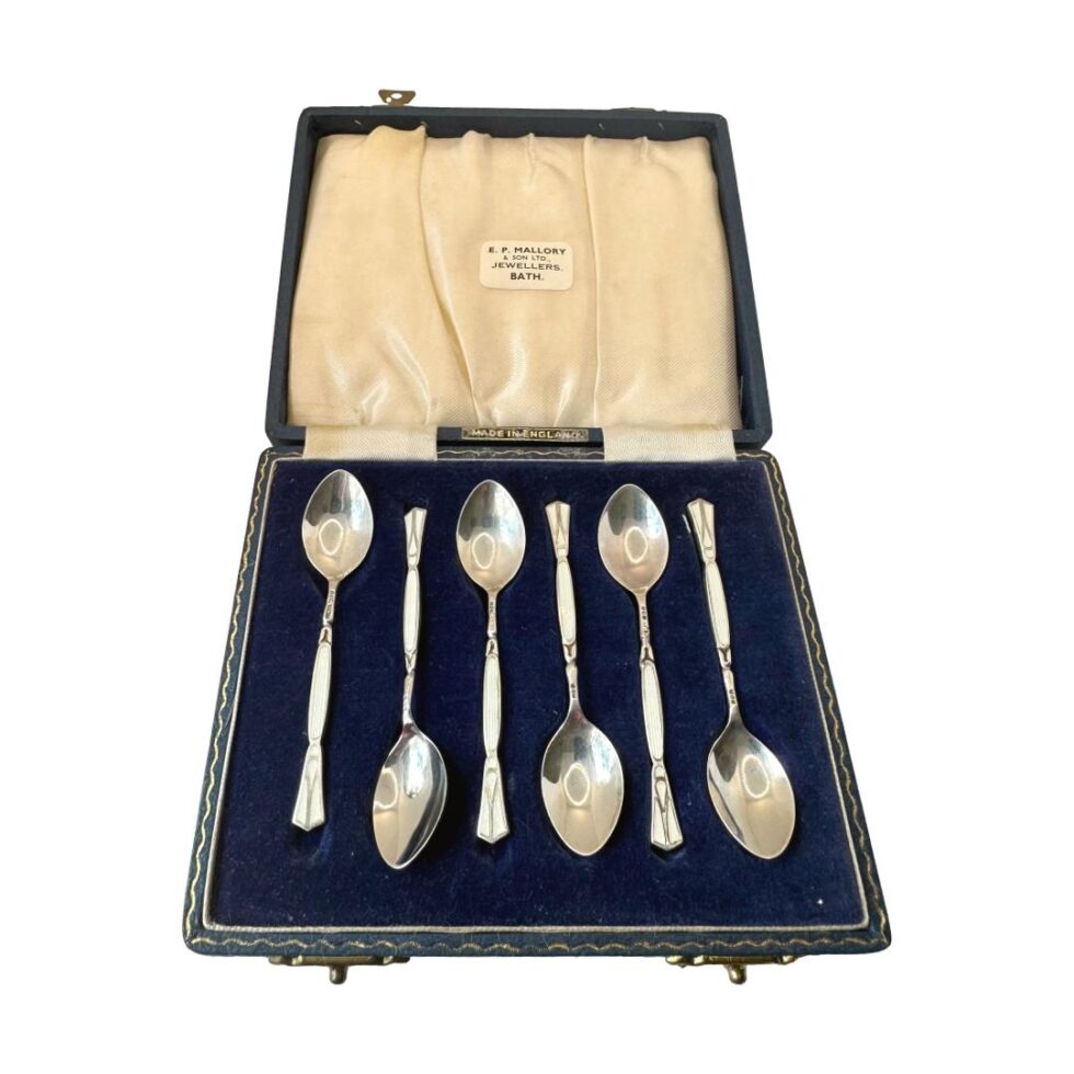 Photo of all the spoons displayed inside their case with the spoon bowls face up. There is some enamelling to the handle at the front.