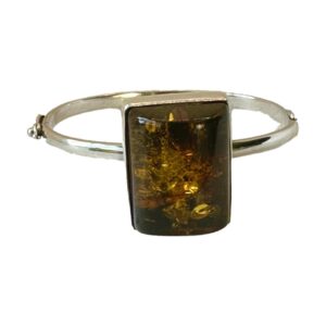 Main photo of Modernist Czech amber bracelet seen with the large amber in the centre foreground. The bracelet, which has quite a thin band in comparison to the large amber has a hinge and hook clasp which makes the bracelet resemble a bangle. The clasp area is just visible to the left.