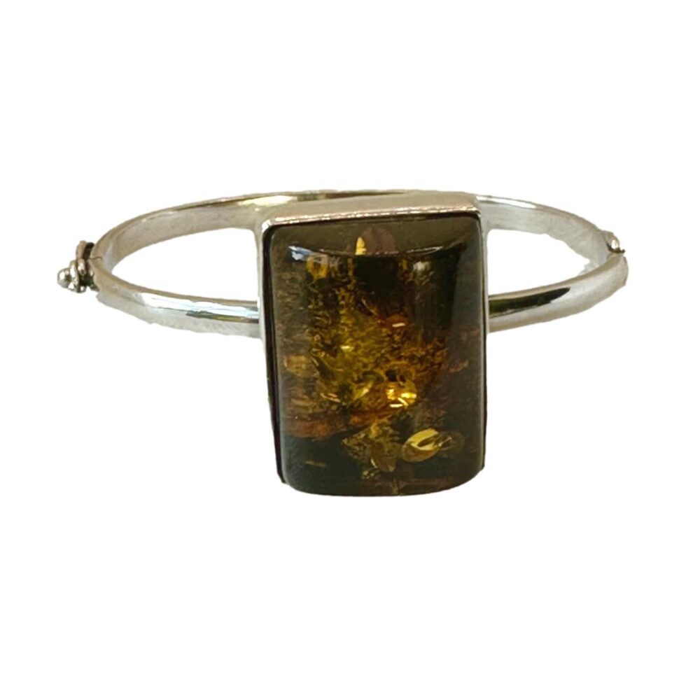 Main photo of Modernist Czech amber bracelet seen with the large amber in the centre foreground. The bracelet, which has quite a thin band in comparison to the large amber has a hinge and hook clasp which makes the bracelet resemble a bangle. The clasp area is just visible to the left.