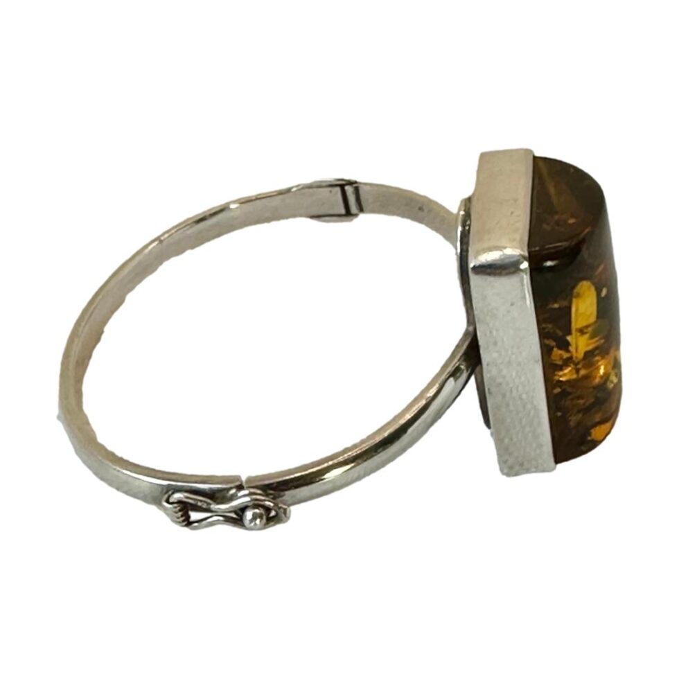 Photo of Modernist Czech amber bracelet seen from the side with the amber on the right. The clasp area is in the foreground (unusually on the side of bracelet) and the hinge is visible in the background. The amber, in comparison to the bracelet looks humungous in size.