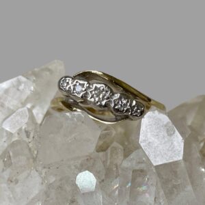 Main photo of gold platinum diamond ring displayed on top of a rock of natural quartz crystal and seen with ring front facing forward. The gold band is split with each end curved over the diamonds which are set in platinum at the centre. The ring is displayed on top of a rock of natural quartz crystal.
