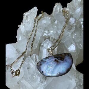 Main photo of opal diamond pendant &chain displayed on top of a rock of natural quartz crystal. The pendant is to the lower right with the front on view. This is a lovely natural opal stone set in pendant form with a diamond in the bail. The natural boulder opal is a semi circular shape with the widest flat connecting to the bail so curved half of semi circle is at bottom. The gold chain has been draped over the crystal with the clasp end visible in lower left corner.