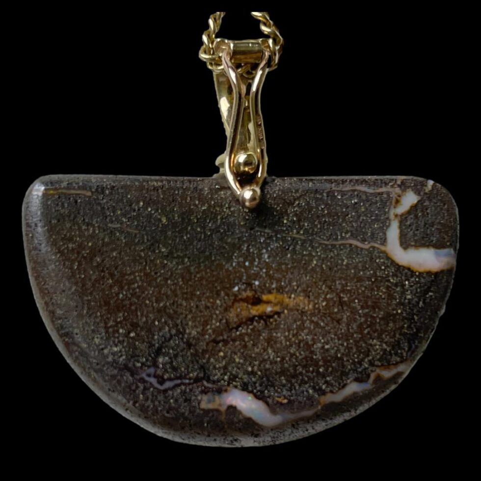 Photo of the back of the boulder opal shown hanging from the chain. The natural stone back is testament to how this piece has been created.