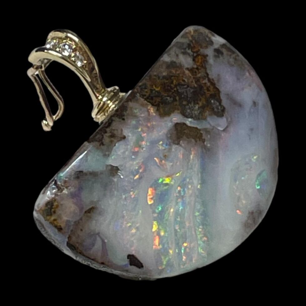 Close up photo of the boulder opal pendant only. The pendant is displayed diagonally across the page with the clasp shown open in the top left corner. There are some beautiful neon like colours emanating from parts the stone.