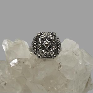 Main photo of adjustable silver marcasite ring displayed on top of a rock of natural quartz crystal with the ring front forward facing. The ring has a minimalist design of a squarish front with a small number of marcasite pieces set within. At the front, each marcasite has its own silver setting including a diamond shaped central frame also with marcasite.