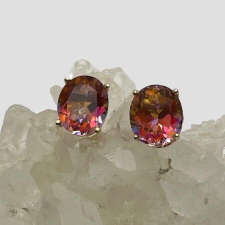 Main photo of mystic topaz 14kt studs displayed on top of a rock of natural quartz crystal with the earrings forward facing. The colours from these stones is amazing, in this photo they are primarily pink with orange and lilac flashes.