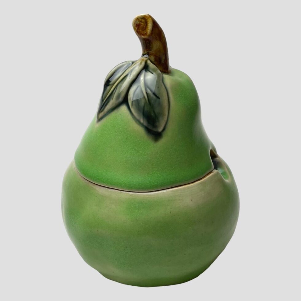 Main photo of Doulton pear preserve pot seen from an eye level. The pear is a green colour with short brown stalk ad 2 darker green leaves at the top. The lid is proportionate to the bottom half.