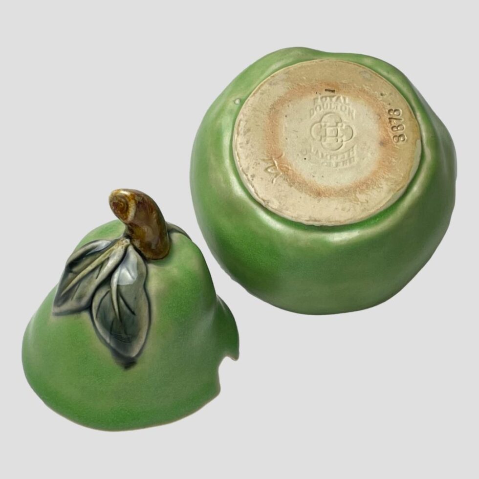 Photo of Doulton pear preserve pot displayed with lid removed and placed on left and the base displaying on the lower part of pot. The debossed Doulton stamp and artists initials VH are visible.