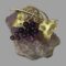 Main photo of signed amethyst grapes brooch displayed balanced on top of a small rock of amethyst. The grape bunch is made up of 10 round amethyst stones with larger ones at top graduating down to smallest at the tip. The amethyst colour is a deep purple. The bar of the brooch is the stalk which has vine coiled around it with a textured vine leaf on either side of the grapes. The gilt of the stalk, vine and leaves and the deep purple of the grapes compliment each other perfectly. A wonderful gift for a wine lover!
