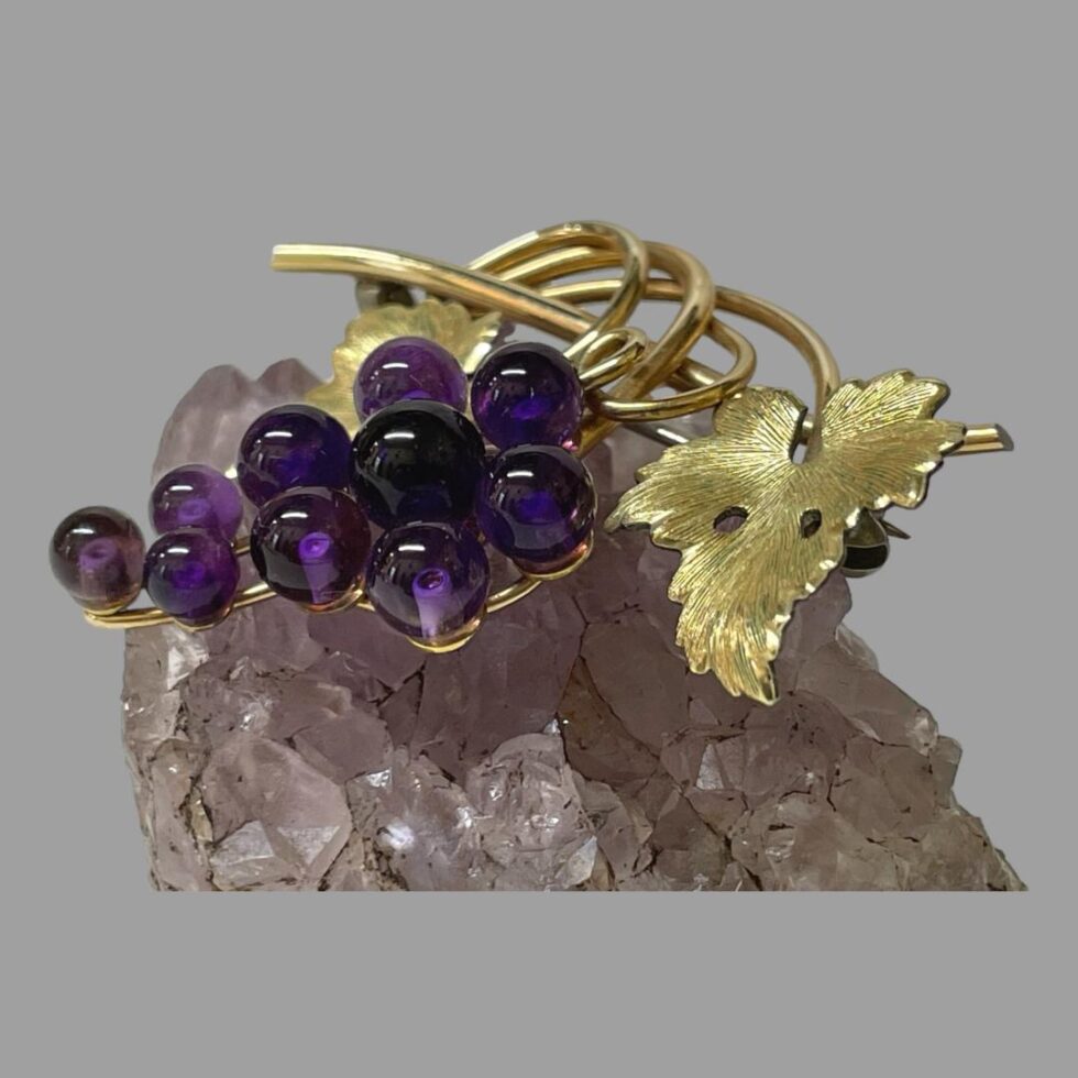 Photo of amethyst grapes brooch still displayed on a piece of amethyst this time seen from a more sidewas angle to show the depth.