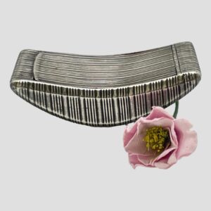 Main photo of George III snuff box seen from a side view with the curved base at the bottom. The box is a smile shape for want of a better description with lovely engine turned detail throughout. There is a single pink faux flower to the bottom right of the photo.