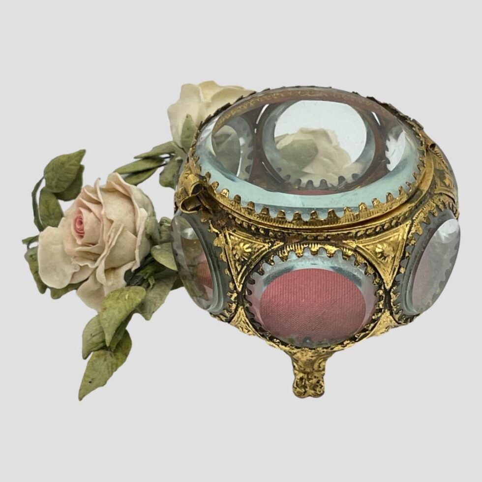 Photo of bijouterie casket this time taken from a little height and looking diagonally down at the circular top. The posy of faux pink roses is visible to left.