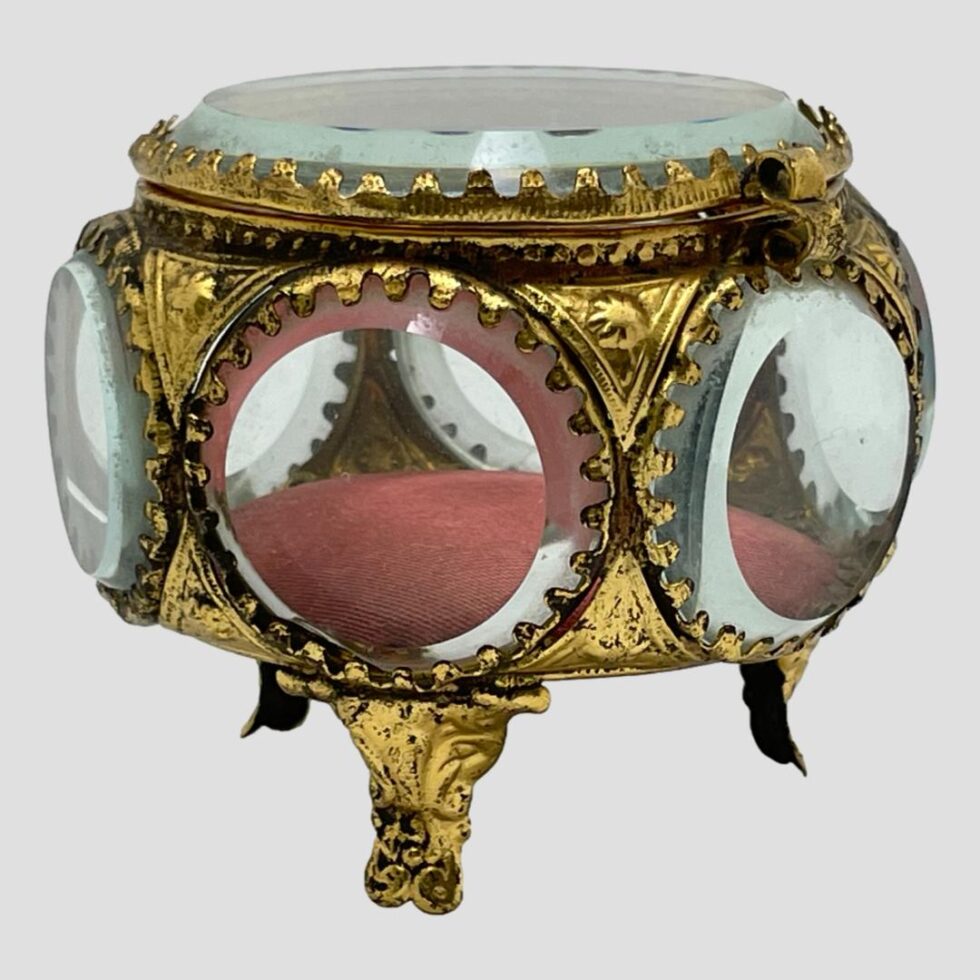 A closer look at the antique French bijouterie casket again from an almost eye level. The red silk padded cushion is visible on the inside. The bevelled glass windows look like portholes on a submarine giving an air of Jules Verne to the box. The 3 tripod feet are all visible, one in foreground and 2 at back. The lovely gilt work around each window creates a stunning box fit for royalty.