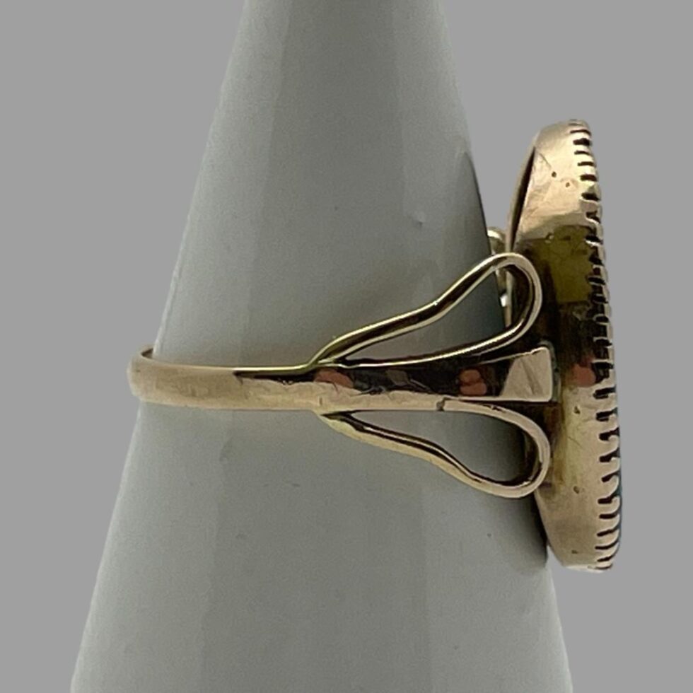 Photo of ring displayed on a cone shaped stand and facing extreme right. As the stone is flat, it is only possible to see the gold band, winged shoulders and frame of stone setting here.