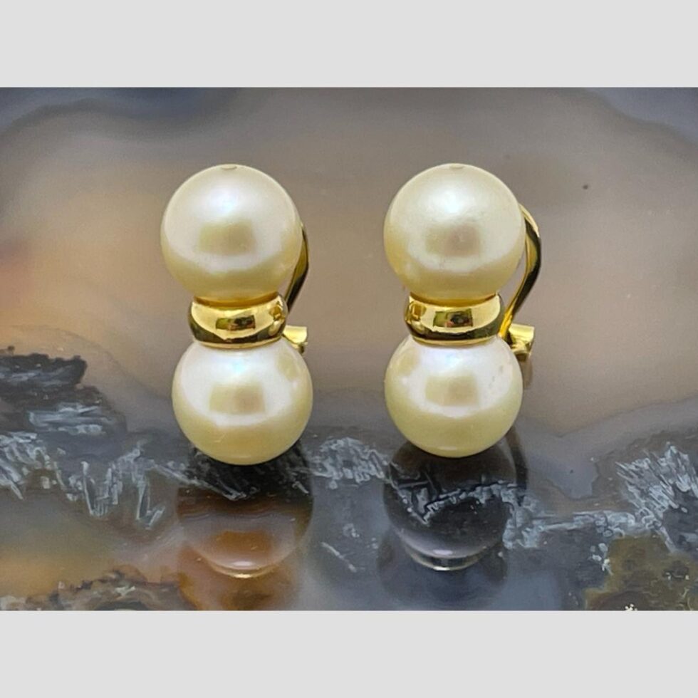 Main photo of gold & pearl clip-ons displayed on top of a slice of natural agate with the earring fronts forward facing. The pearls are set one above the other with a gold divider. A little like a figure of eight with an elongated mid section...in gold! These earrings look stunning when worn.