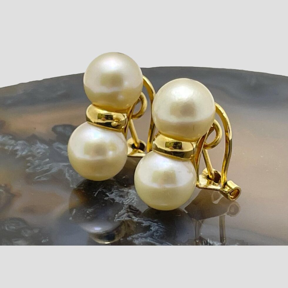 Photo of the double pearl earrings still on slice of agate with the earring fronts facing towards the bottom left corner. The pearls are a fairly generous size. Part of the clips can be seen.