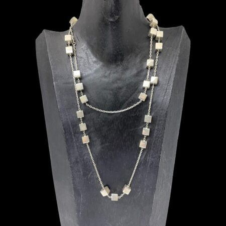 Main photo of Georg Jensen Aria necklace displayed on a black wooden stand and forward facing. The necklace has been doubled up for this photo as it very long. The long chain has groupings of silver cubes in 2's, 3's and even solo. It is possible to see the random spacing of the cubes on this necklace - there is no distinct pattern as to their arrangement.