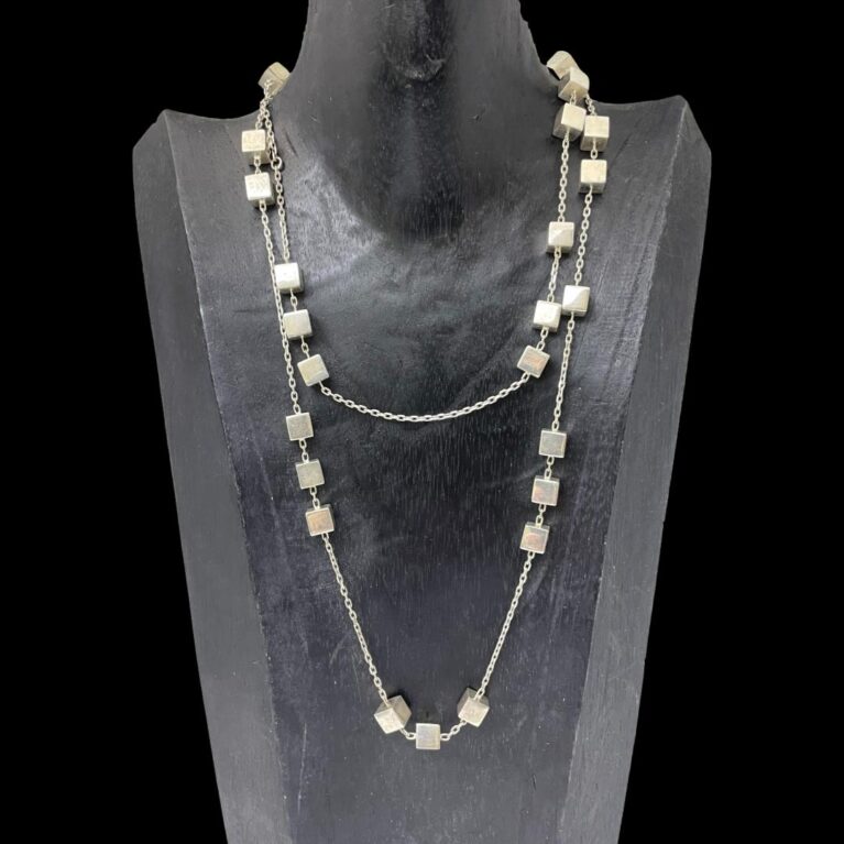 Main photo of Georg Jensen Aria necklace displayed on a black wooden stand and forward facing. The necklace has been doubled up for this photo as it very long. The long chain has groupings of silver cubes in 2's, 3's and even solo. It is possible to see the random spacing of the cubes on this necklace - there is no distinct pattern as to their arrangement.