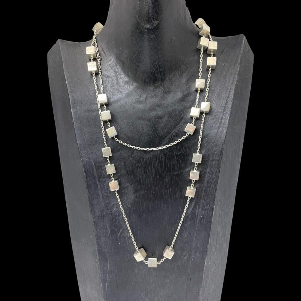 Main photo of Georg Jensen Aria necklace displayed on a black wooden stand and forward facing. The necklace has been doubled up for this photo as it very long. The long chain has groupings of silver cubes in 2's, 3's and even solo. It is possible to see the random spacing of the cubes on this necklace - there is no distinct pattern as to their arrangement.