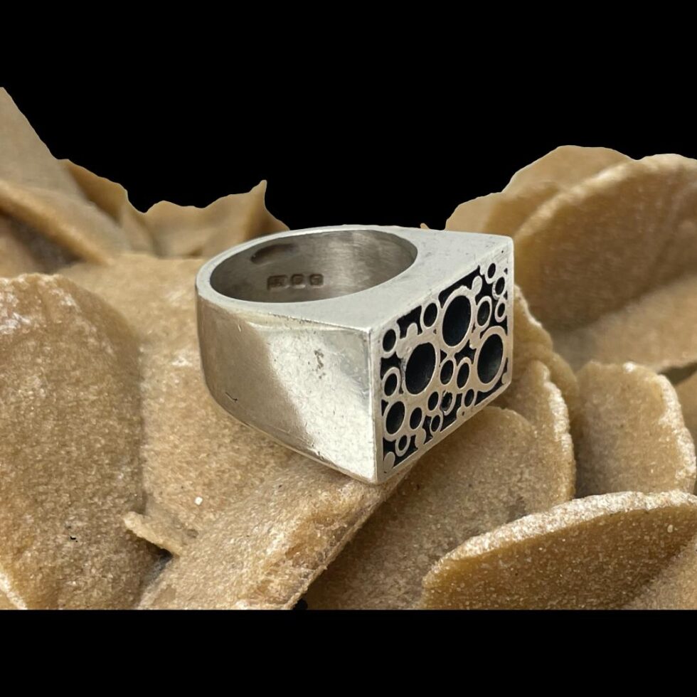 Photo of Modernist Brutalist ring still displayed on a rock of natural desert sand rose this time with the ring front facing towards bottom right corner.