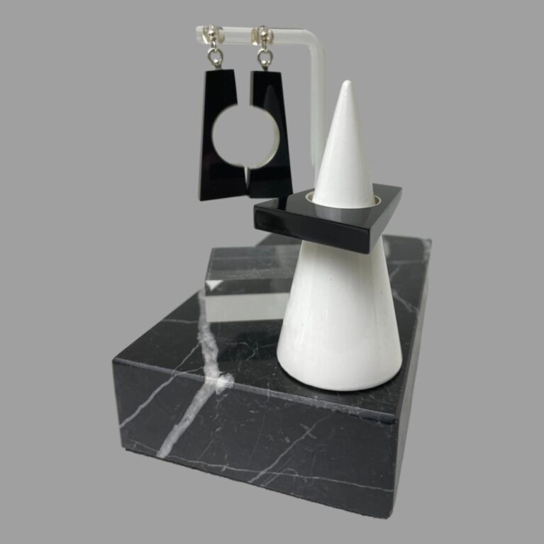Main photo of 60s style earrings and ring set displayed together with the ring on a cone shaped white stand which is on top of a block of black marble. To the back left, the earrings are hanging from a Perspex stand. The earrings, when put together are the exact same size and shape as the ring. Imagine a pyramid with the pointed top lopped off and a circle in the centre which is then cut in half. That is the earrings. The ring is obviously not cut in half! The earrings have silver posts and lined with silver on the inside of the semi circles. The ring has just the silver lining on the inside of circle. Hallmarked to all 3 pieces.