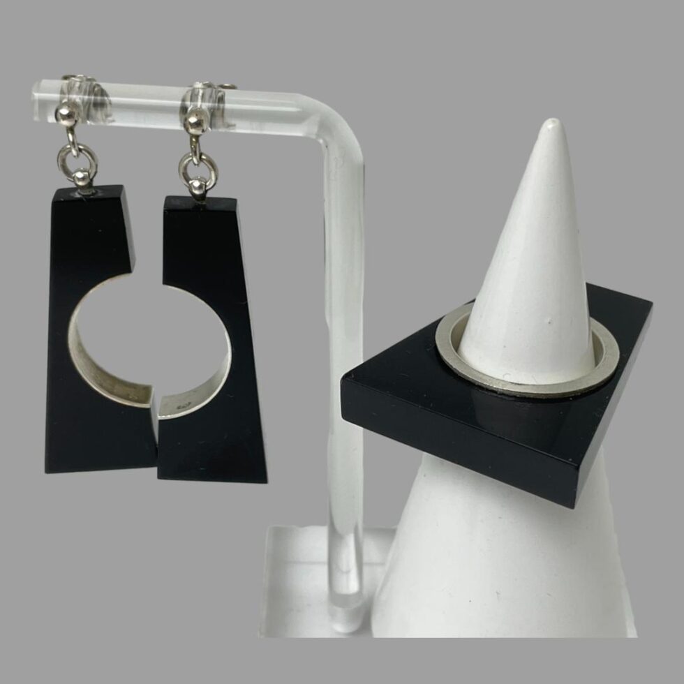 A close up of the earring and ring set with earrings still on the Perspex stand and to the left and ring on the cone shaped stand and on the right.