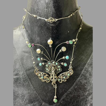 Main photo of antique French peacock necklace displayed on a black wooden display stand and forward facing. The chain has been wound round the neck once so the clasp area is at the top centre. The peacock takes quite a large area of this necklace with its width and length. It would look fabulous worn with a low fronted dress.