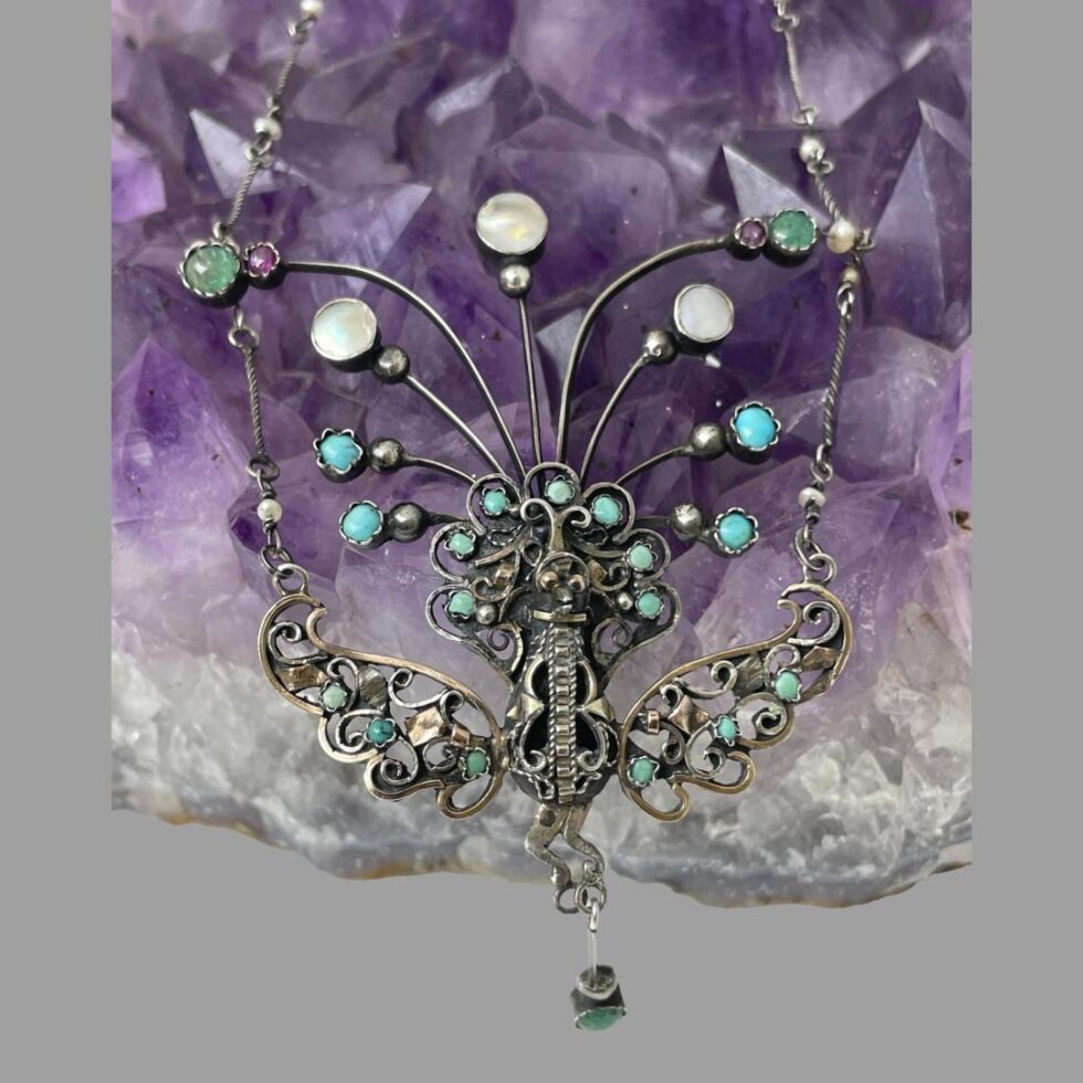 Photo of the peacock area of necklace again this time laid on a rock of natural amethyst. Against the purple of the amethyst, the colours of the stones used within the peacock stand out a great deal.