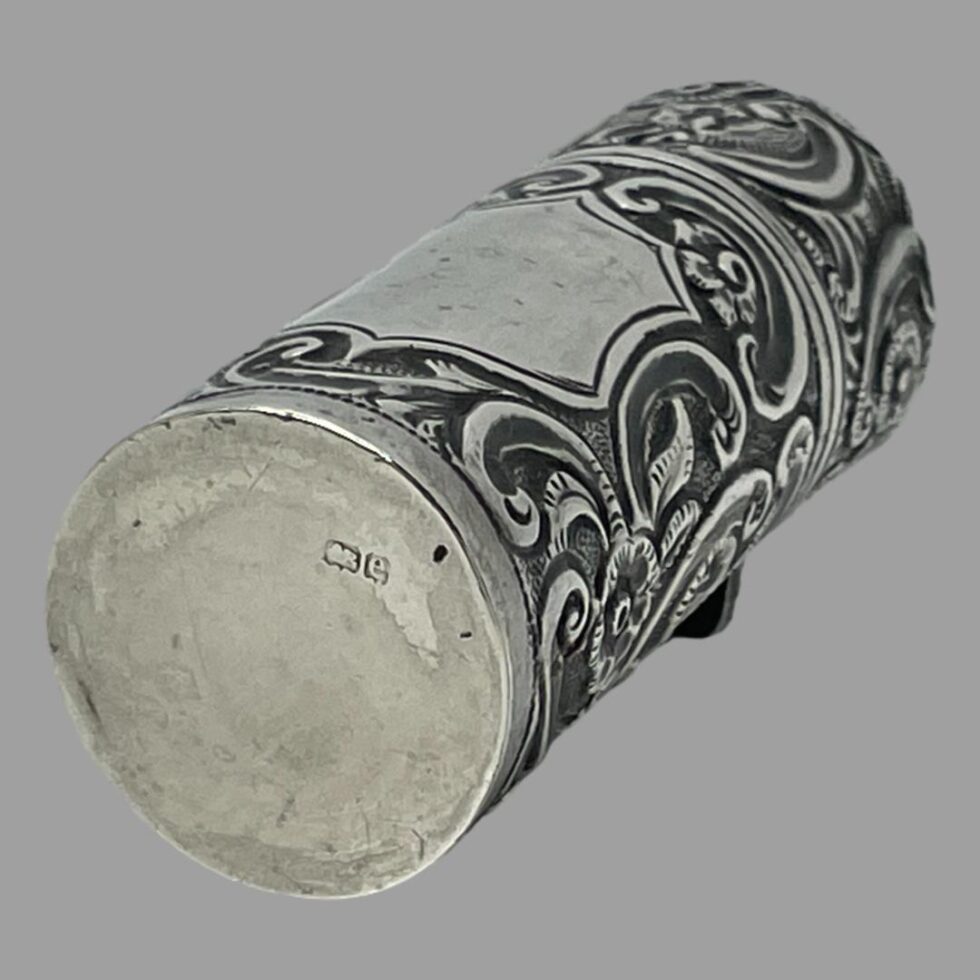 Photo of portable silver perfume bottle displayed on its back with cartouche area at top. There is a short hallmark of lion passant and date letter e to the base.